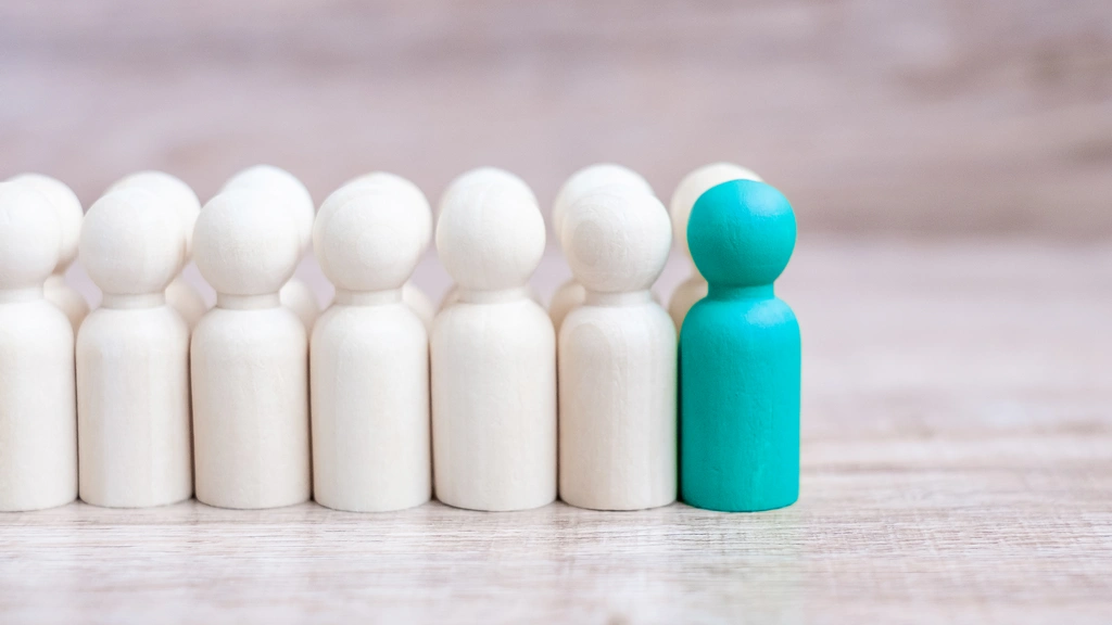 Row of wooden figures with one painted turquoise standing out, symbolising individuality and leadership.