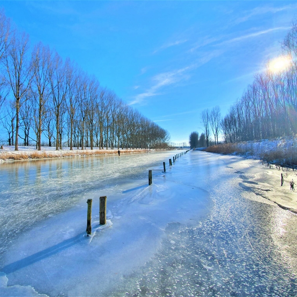 A frozen canal against a clear blue sky in the Netherlands.